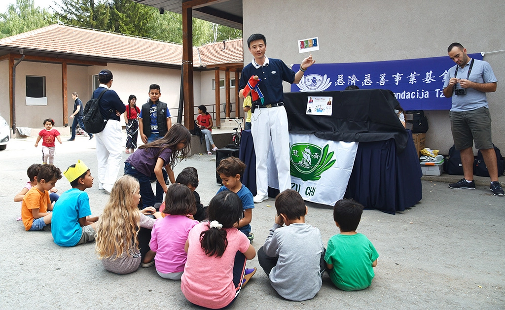 歐洲慈濟志工長期關心滯留在塞爾維亞的各國難民;慈濟志工發放新書包和文具用品給難民孩子。林正中師兄(惟揚,中)帶來布袋戲木偶劇,透過活潑可愛的表演,帶動小朋友如何分類做環保,所有的小朋友都吸引過來,大家席地而坐。