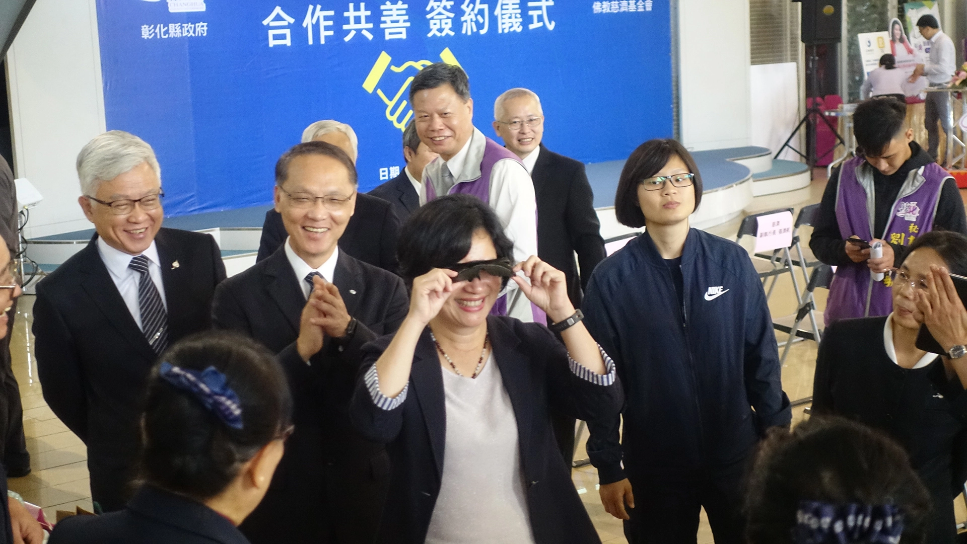 顏博文執行長介紹慈濟用寶特瓶製成的生活用品,王惠美縣長立刻試戴太陽眼鏡。