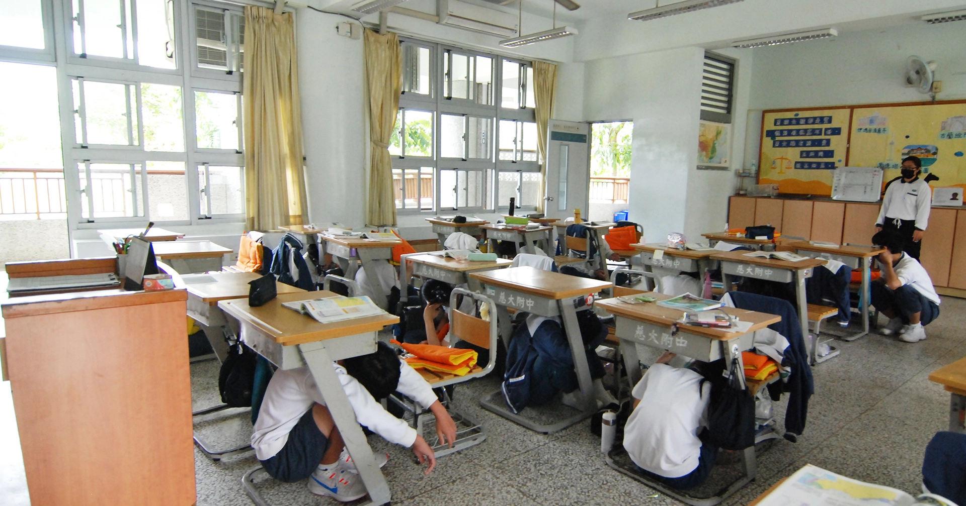 慈大附中全校師生進入地震模擬情境,師生躲在桌下、柱旁或牆邊,等地震稍歇後,由師長引導學生快速至運動場集合。