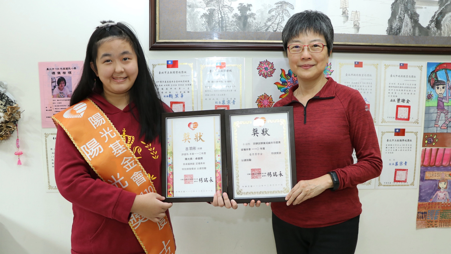 陽光基金會執行長舒靜嫻親自到宅為陽光獎得主古羽彤(左)頒獎,在家人布置得滿牆獎狀跟畫作前合影