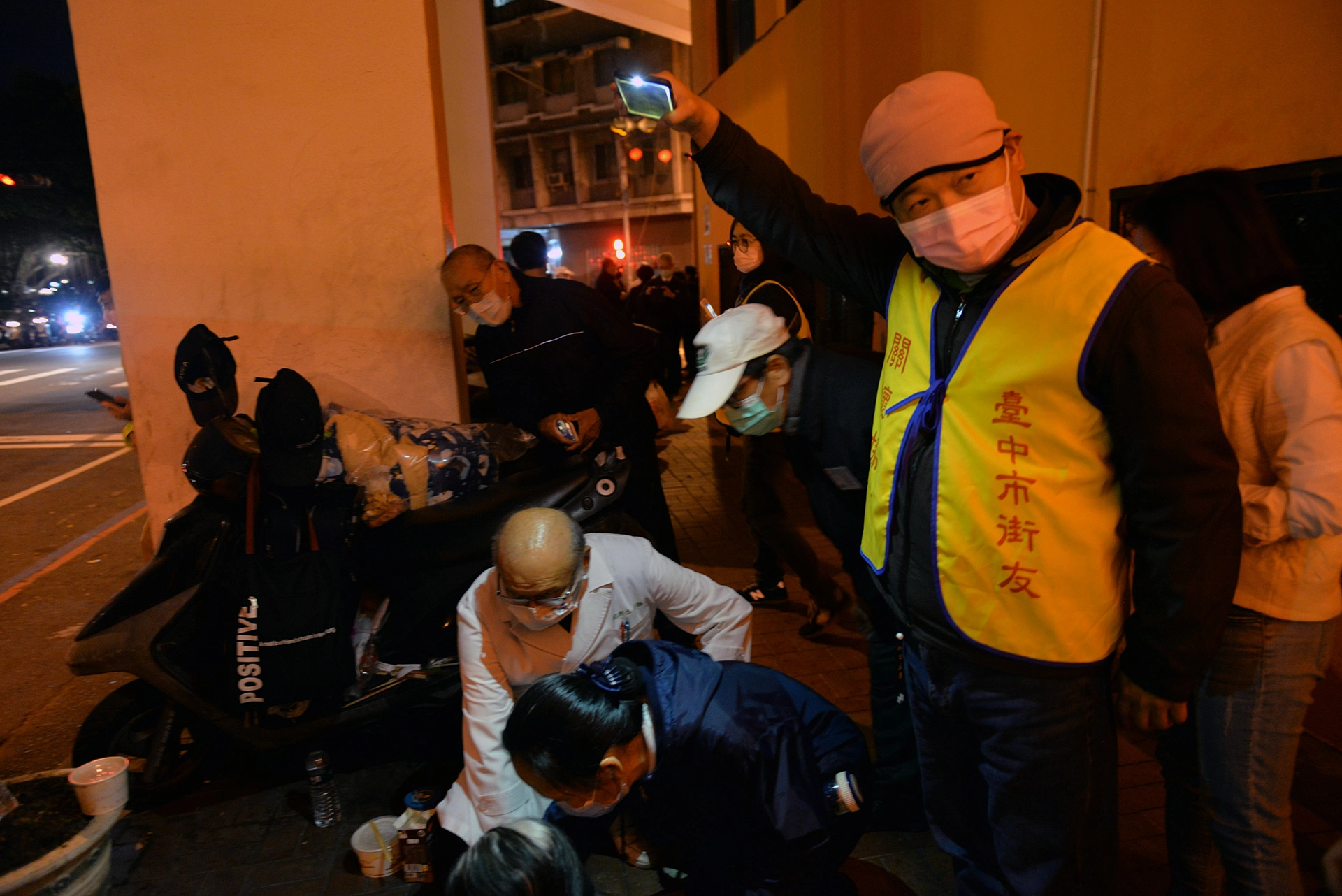 台中市街友關懷協會何志成理事長(右)用手機幫人醫會醫護人員照明。