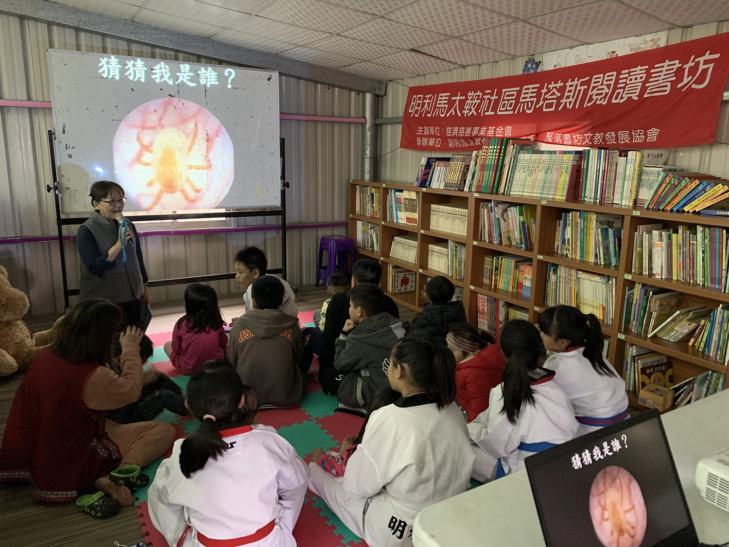 聚落書坊理事長王緯華說故事〈塵螨丁丁搬家記〉,不只孩童聽得津津有味,窗戶旁的家長也聚精會神專注聽。(攝影:徐靖雯)