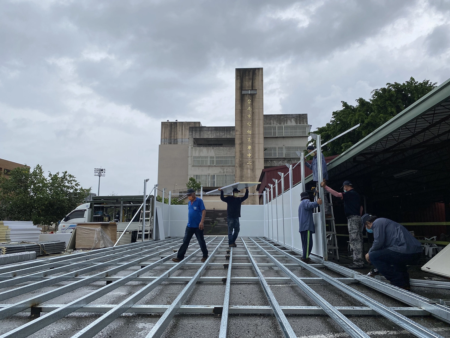 5月30日在松柏育樂中心搭建篩檢組合屋,營包商雨中施工希望趕緊搭建完成。(攝影:吳珮婕)