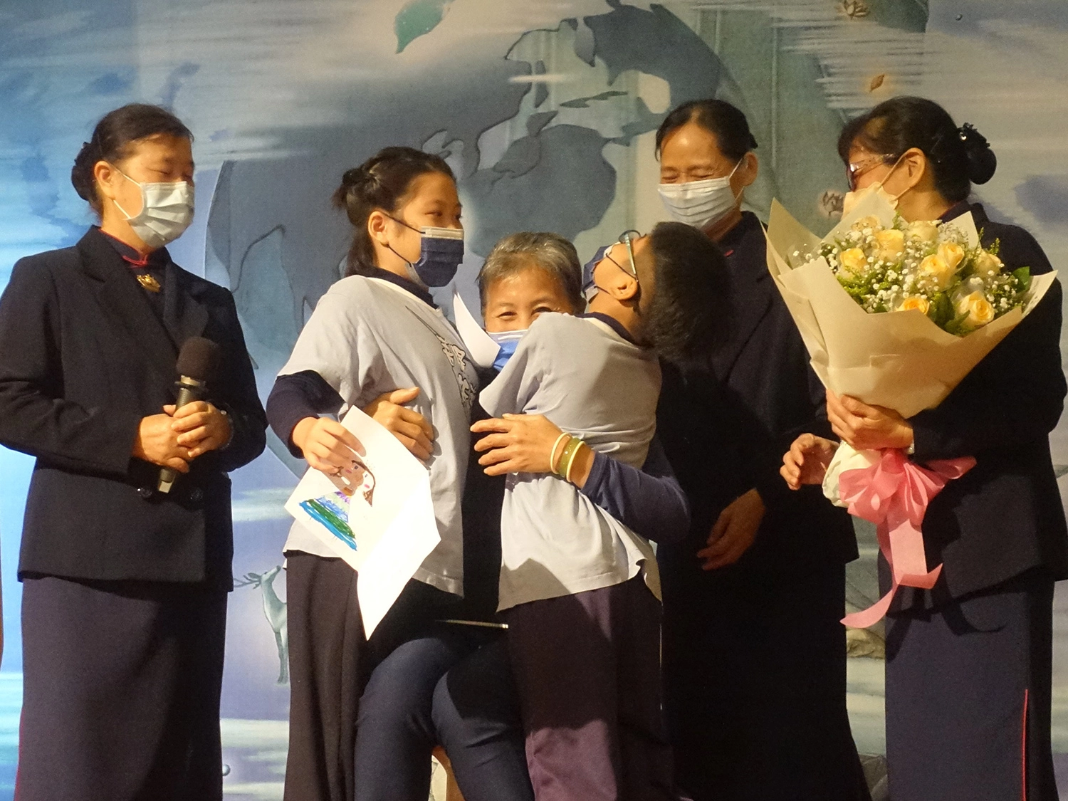 台東慈濟12月31日舉辦冬令發放活動,照顧戶侯女士與孫子上台分享,孫子孫女擁抱她感恩教養之恩。(攝影:陳誼謙)