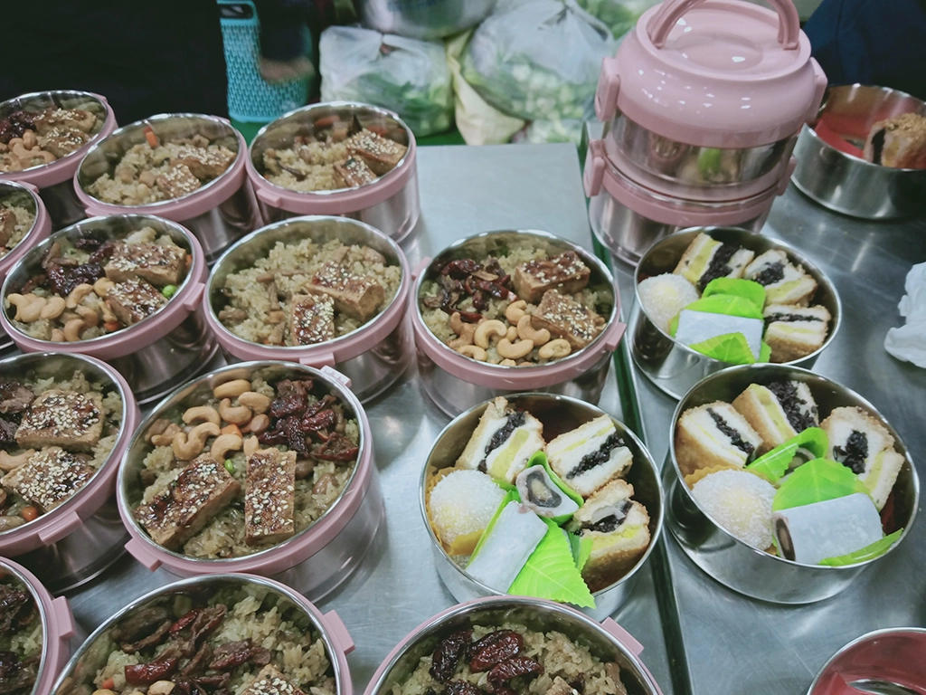 志工將蔬食年菜放入提鍋,讓照顧戶帶回與家人分享,提鍋也可重複使用,宣導環保。