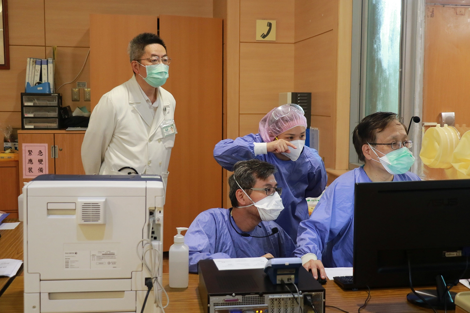 簡守信院長(右)在「65歲以上長者防疫門診」值班,急診室同仁說明電腦操作事宜,其它科醫師也前來觀摩。