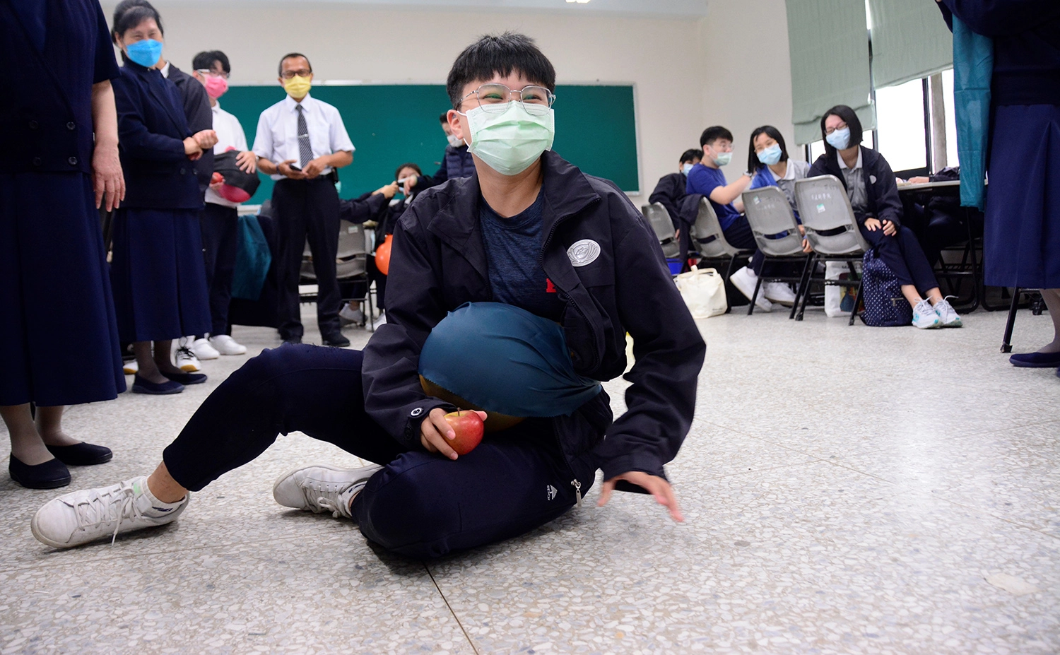 學生在腰上綁上氣球後,還需完成撿蘋果任務,不慎跌坐地板。
