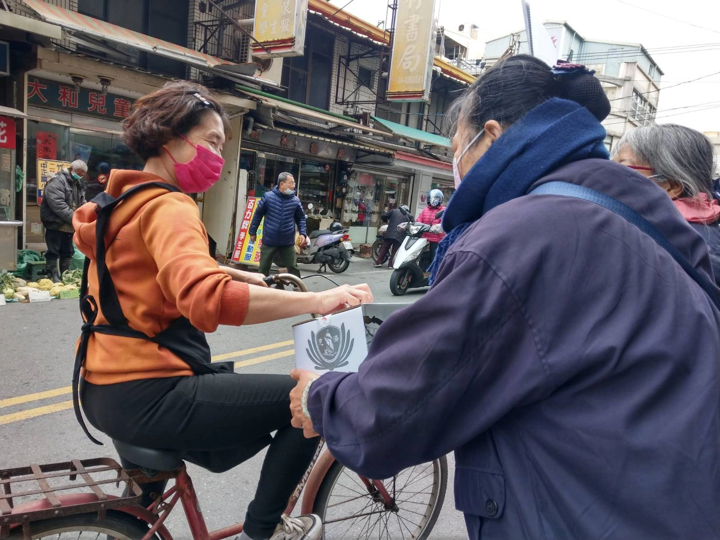 愛心商店的老闆娘得知志工在定點募愛,專程騎單車來投愛心。(圖為慈濟基金會提供)