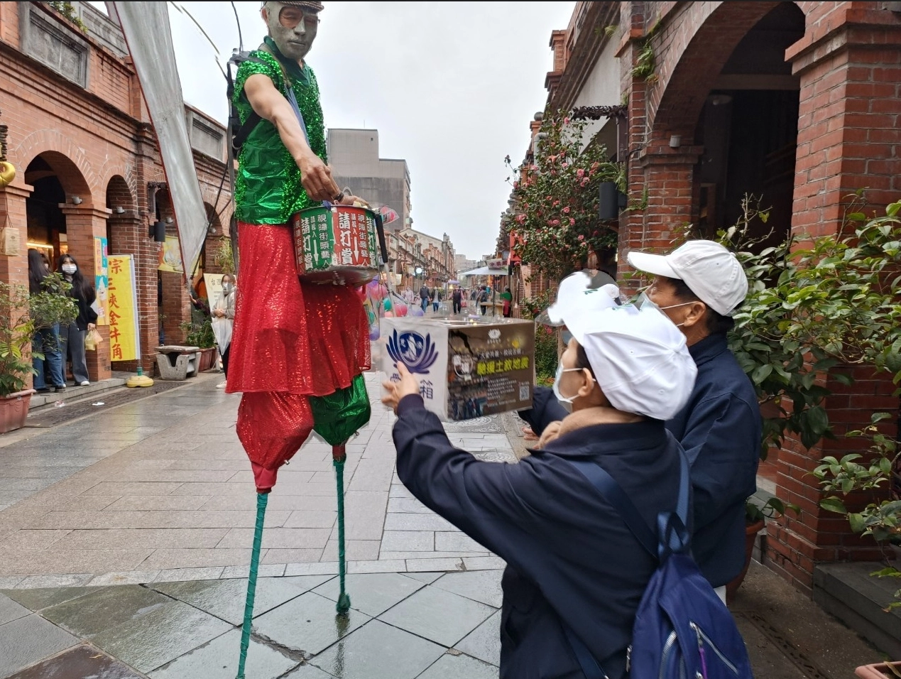 在三峽老街,一位街頭藝人在表演完畢後,踩著高蹺來到慈濟人面前,將他辛苦表演的賞金投入捐款箱。