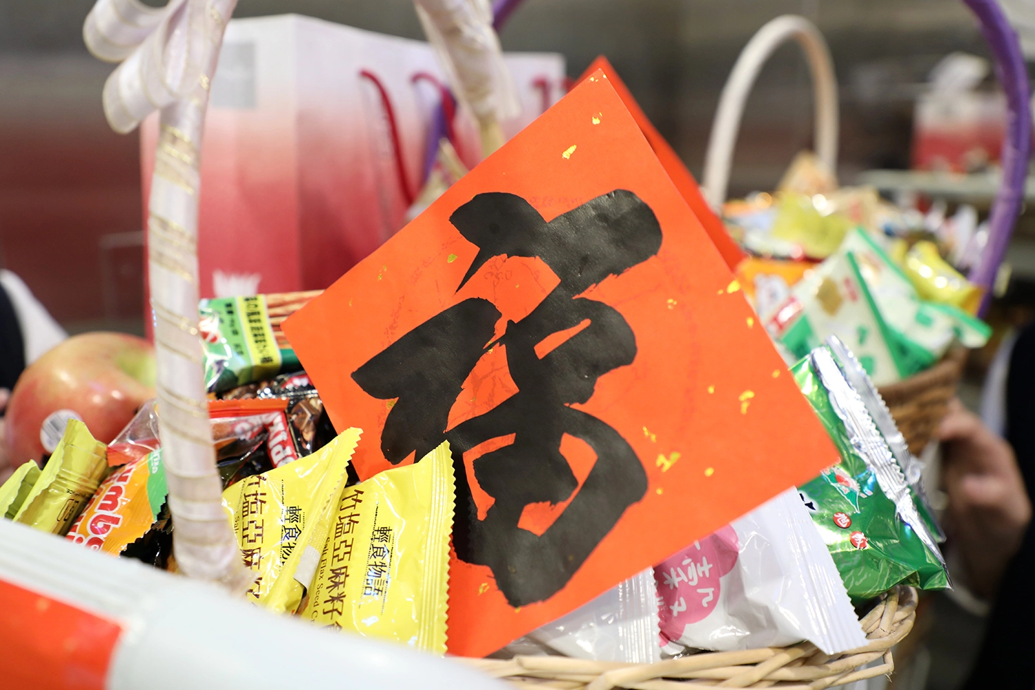 年節提籃裡有象徵「平安」的蘋果、「大吉大利」的橘子、「巧妙克服壓力」的巧克力等糖果餅乾,以及淨斯本草飲、淨斯五穀粉與竹筒,祝福同仁平安過好年。