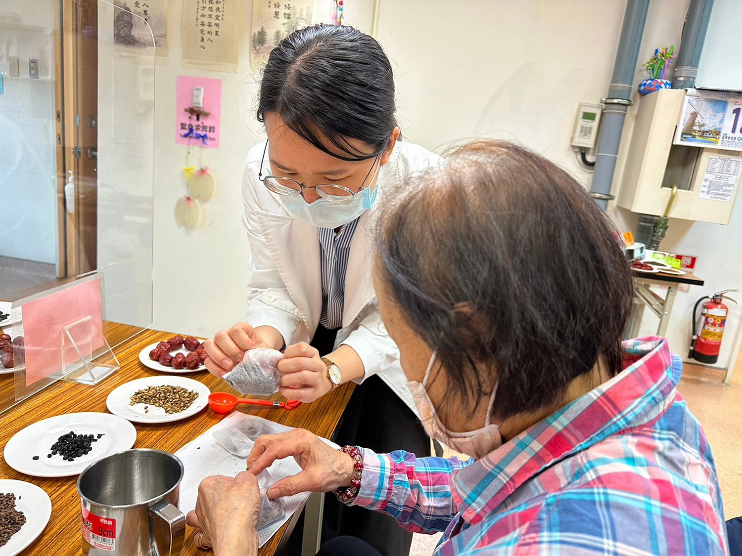鄭宇真醫師(左)為長輩示範將藥材裝入茶袋中。