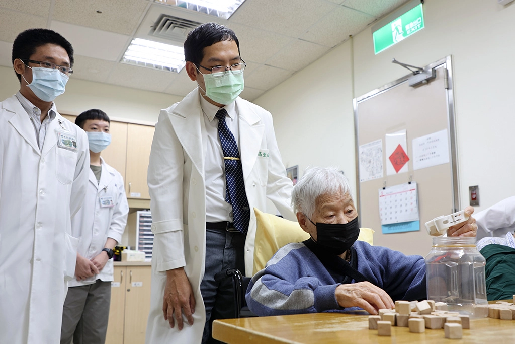 楊奶奶積極復健,練習單手用夾子將積木夾起並放入桶內。