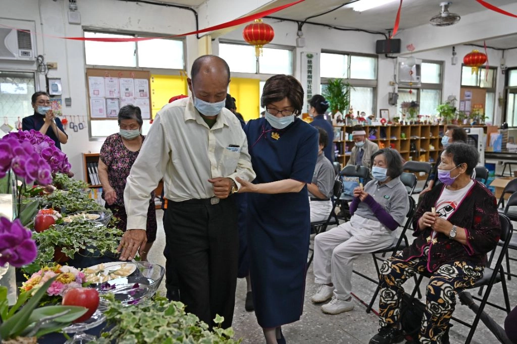 志工王麗卿攙扶行動不便的長者上前浴佛,與長者結緣的蘋果和小盆花是她準備的。