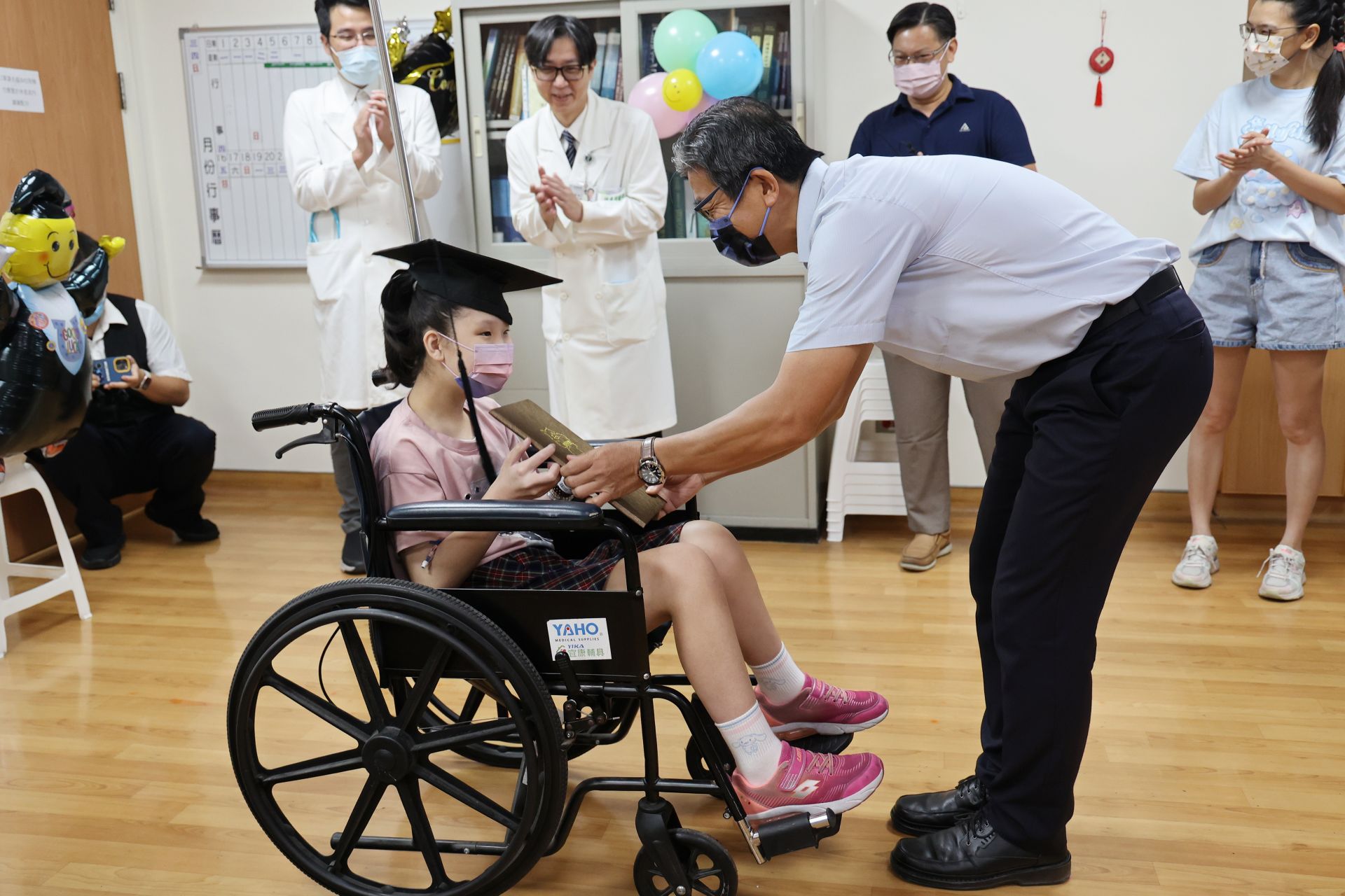 明義國小校長許傳德頒發畢業證書祝賀黃小妹從學校畢業,也從病房畢業,學校導師與師長也一起送上祝福。