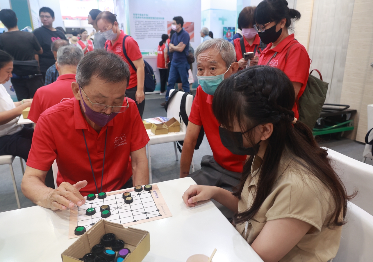 五位失智長者(穿紅衣)及陪同者,展現失智症者練習的成果和讓他們承擔桌長,帶動與會民眾玩環保桌遊。