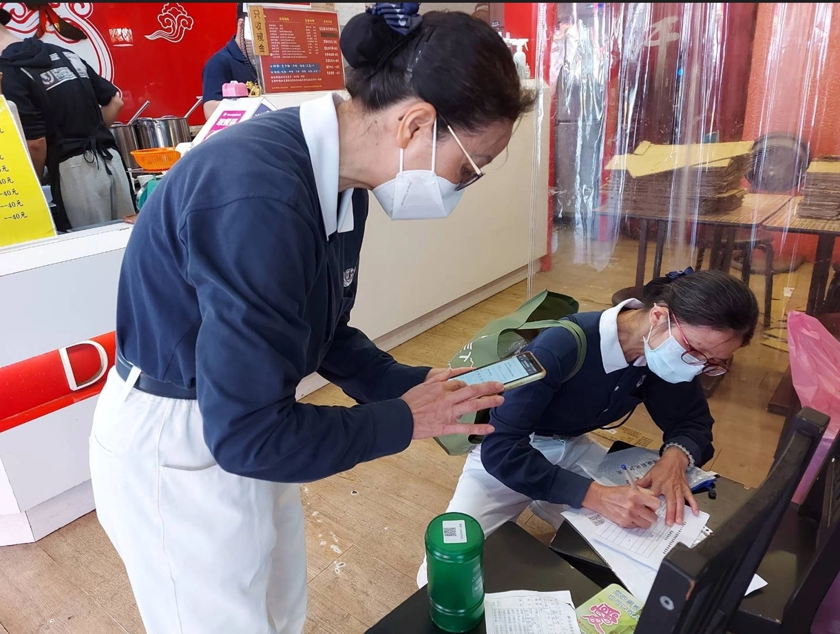 當店家同意放置愛心竹筒,蔡月蘭(左)即掃瞄筒底QRcord上傳店家寶號、地址、電話、推廣人等資料;同時賴春薇(右)將零錢箱收款專用夾鏈袋內零錢箱點收表取出,填寫店家資訊,然後再將竹筒放定位,二人合作無間。