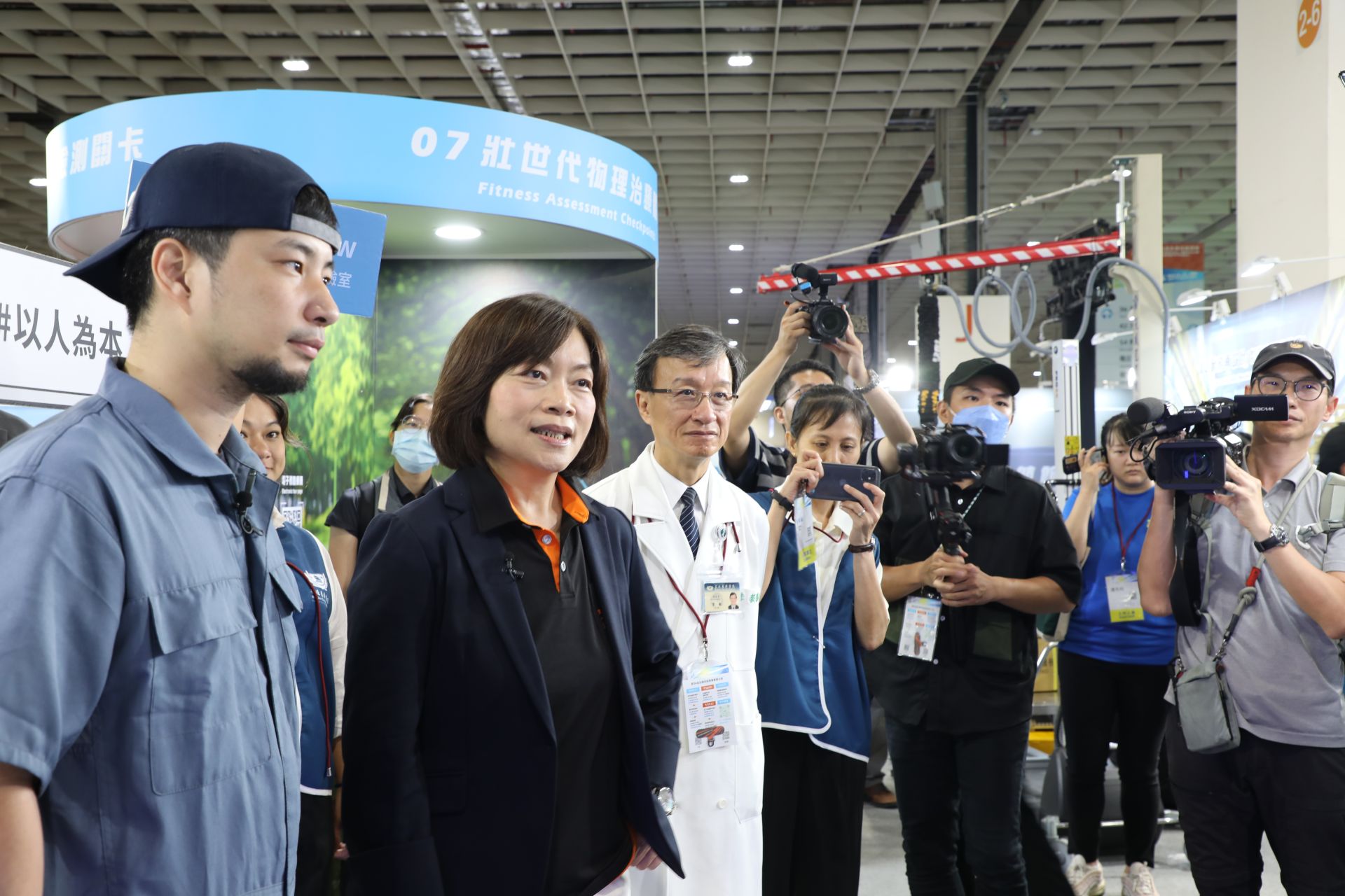 勞動部部長何佩珊(左二)在直播主超認真少年(左一)陪同下,來到「主題展示區」壯世代菁采館展,花蓮慈濟醫院「i菩提x FedGPT」展區。左三圍花蓮慈院醫務秘書李毅醫師。