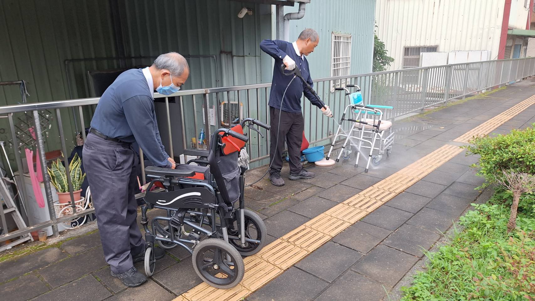 志工蘇國棟(右)將載回來的輔具用洗車的噴槍大力沖洗,做徹底清洗消毒,他表示有做就有福。黃中萬(左)把回收回來的輪椅被套也一起清洗消毒。