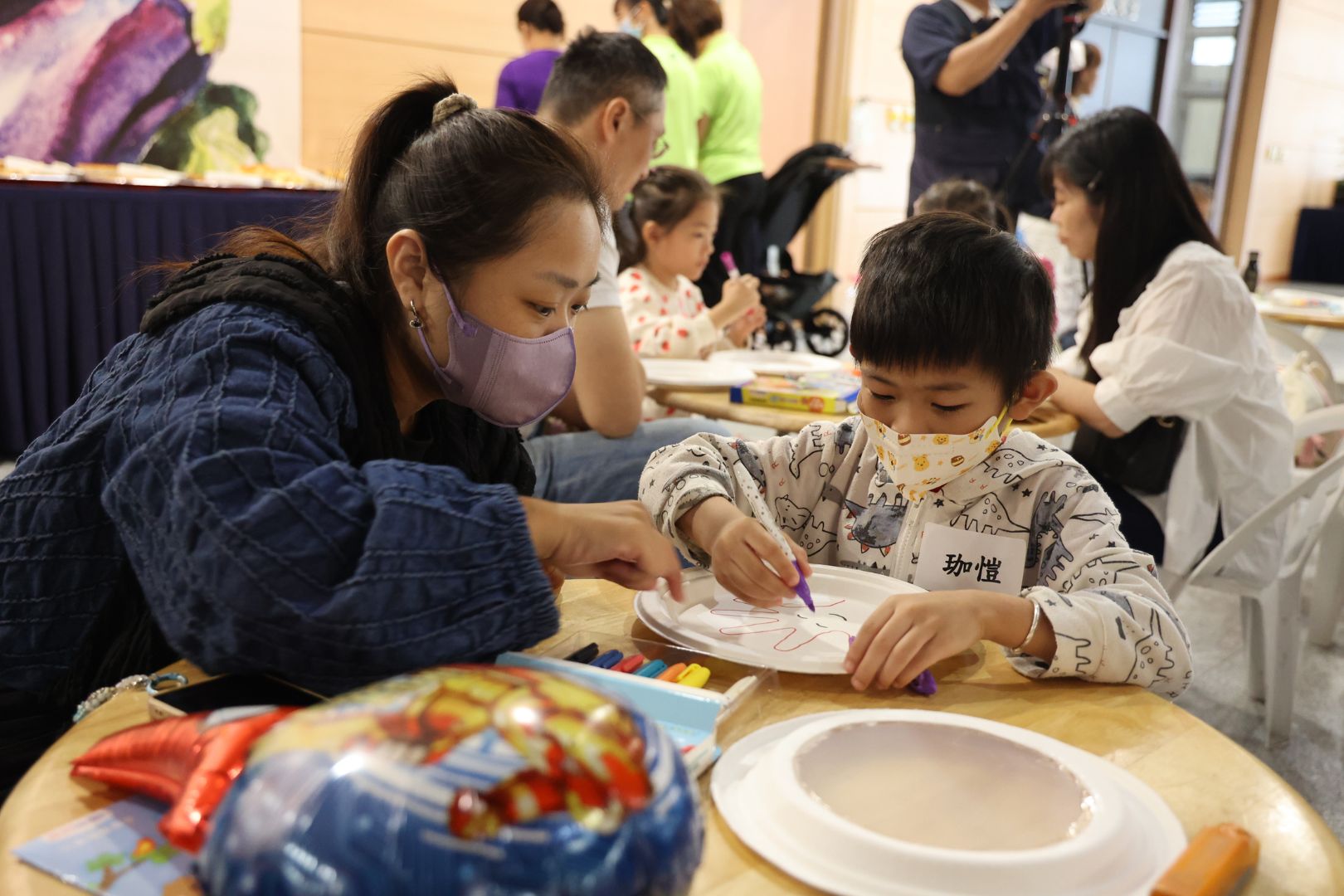 家長帶著孩子用兩個盤子一起作海浪鼓，先在一面盤子上用彩筆記錄孩子的手掌大小。
