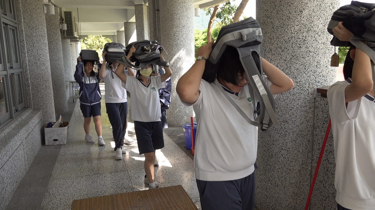 中學部學生從教室疏散時,以書包保護頭部,避免受傷。