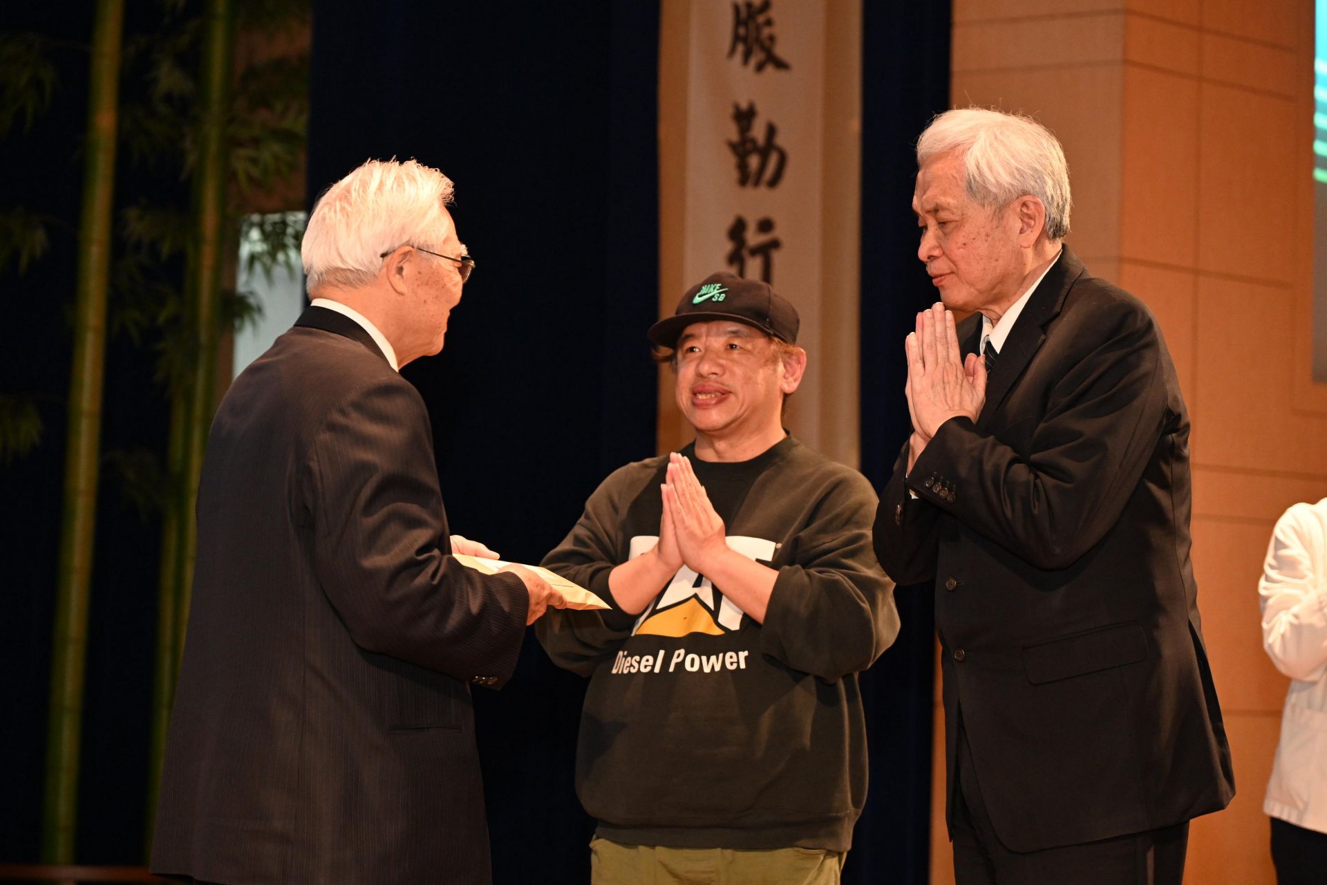 吳弘斌的父親(左)接受王本榮執行長(右)與導演許豐明(中)致贈的紀錄片光碟。