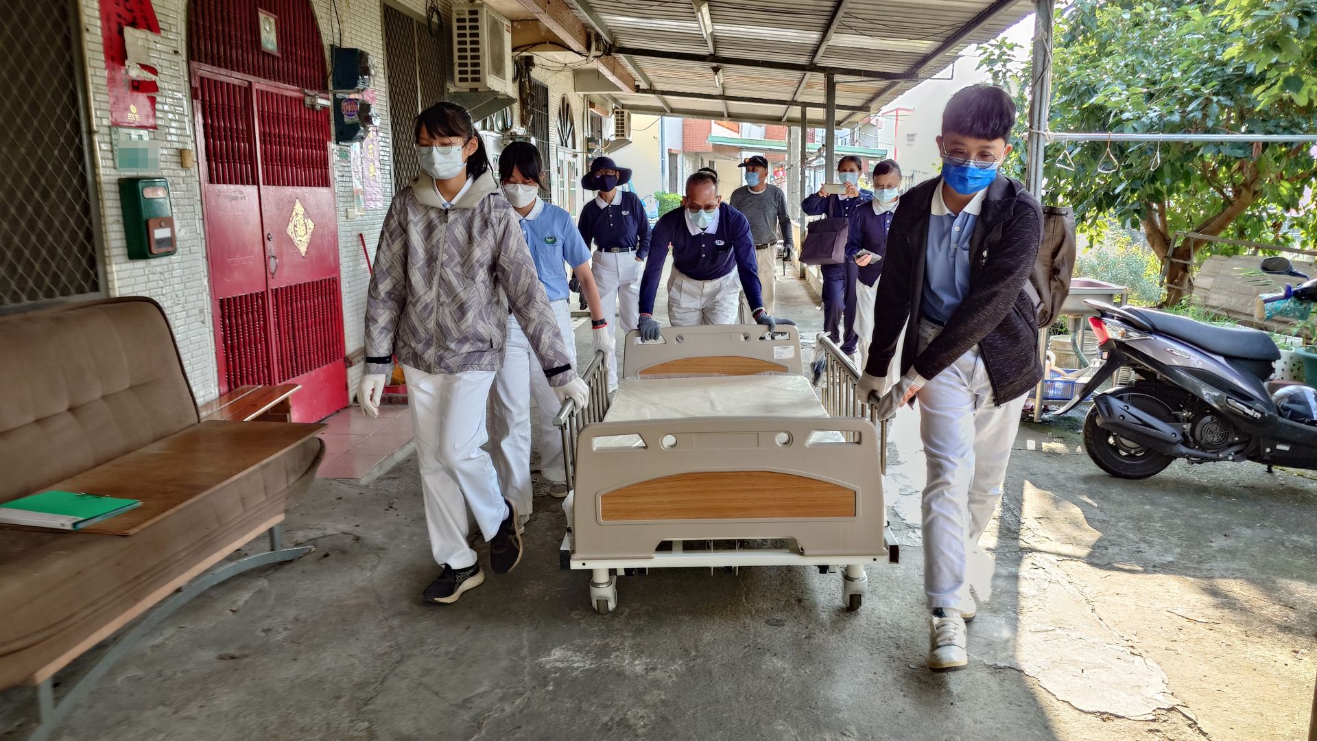 因輔具車無法直達案家門口,學員與志工合力推著近百公斤的病床至案家