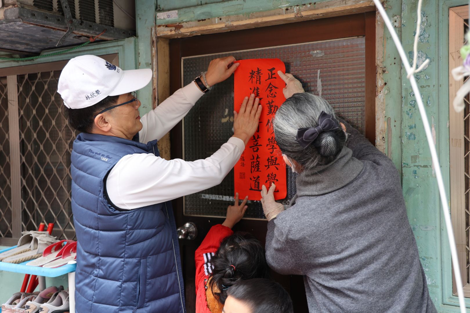林欣榮院長(左)、顏惠美主任(右)與高先生的女兒(中)一同開心地貼上春聯,為高先生一家送上新春祝福。