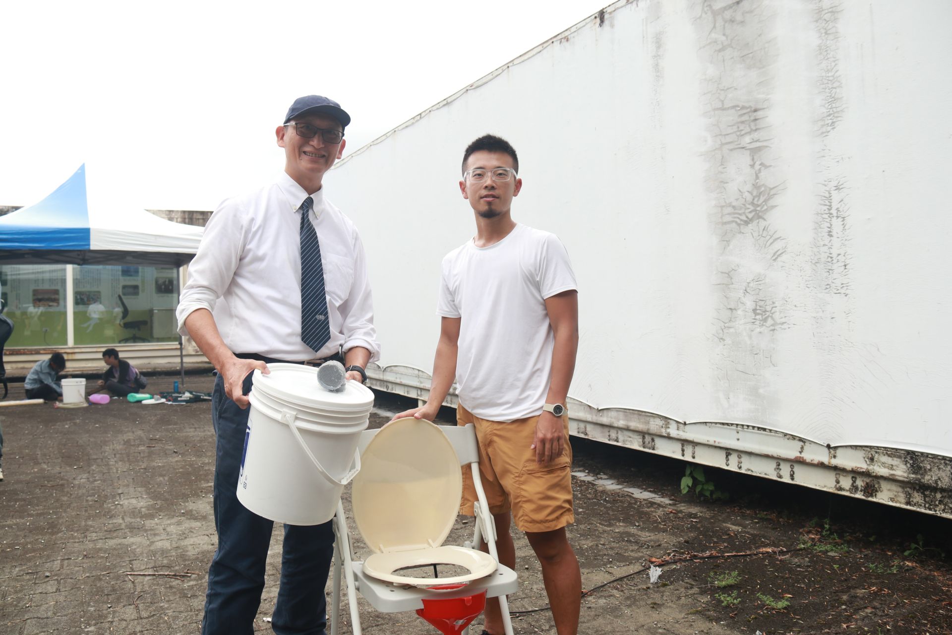學員自己到大賣場買材料製作屬於家庭的乾式廁所,學員許博勛他特別選簡單的材料,只要用束帶,美工刀等身邊找的到的工具,就能做一個簡易的防災廁所。(圖為與邱奕儒老師合照)