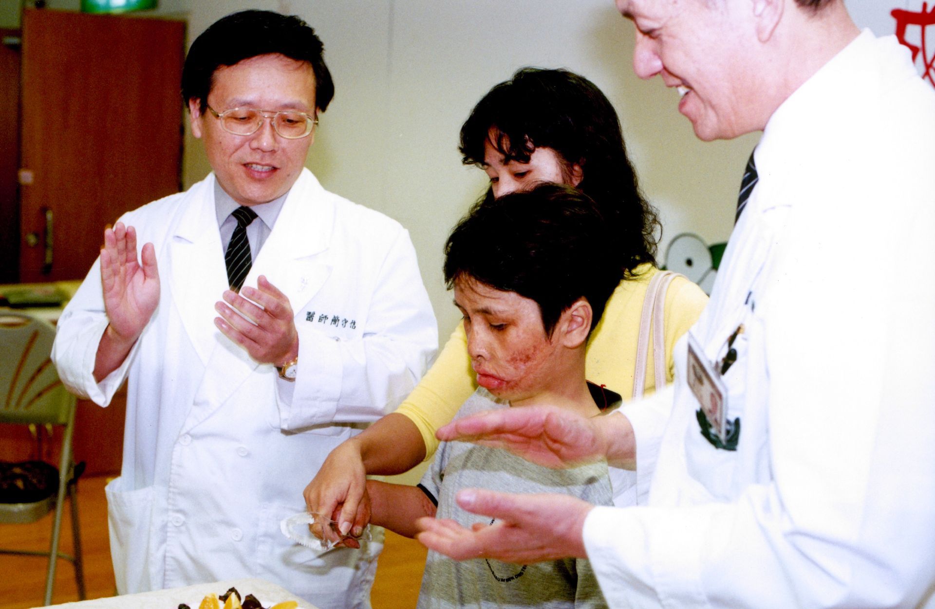 2001年,來自越南的官世成在大林慈濟醫院照顧下恢復走路,在歡送會切下象徵重生的蛋糕。左一為簡守信院長,右一是林俊龍執行長。
