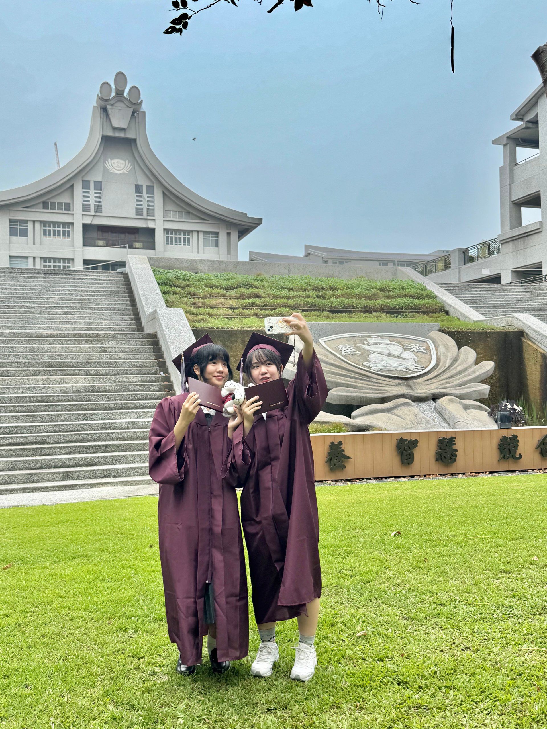 畢業生於校園建築前自拍留念,手持畢業證書,紀錄抛帽時刻。