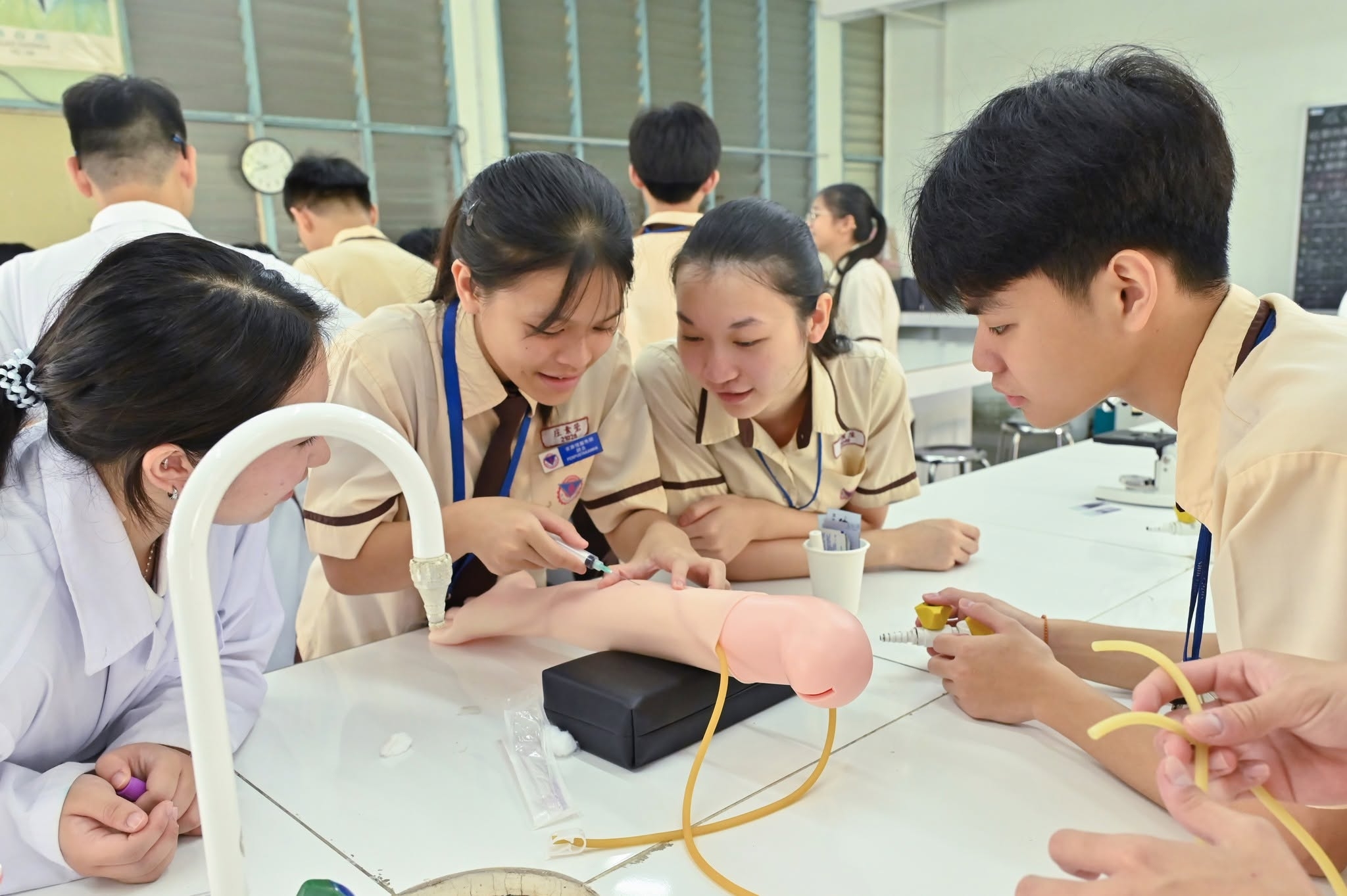 學生專注學習抽血操作，在指導下透過模擬手臂進行實作練習，親手操作。