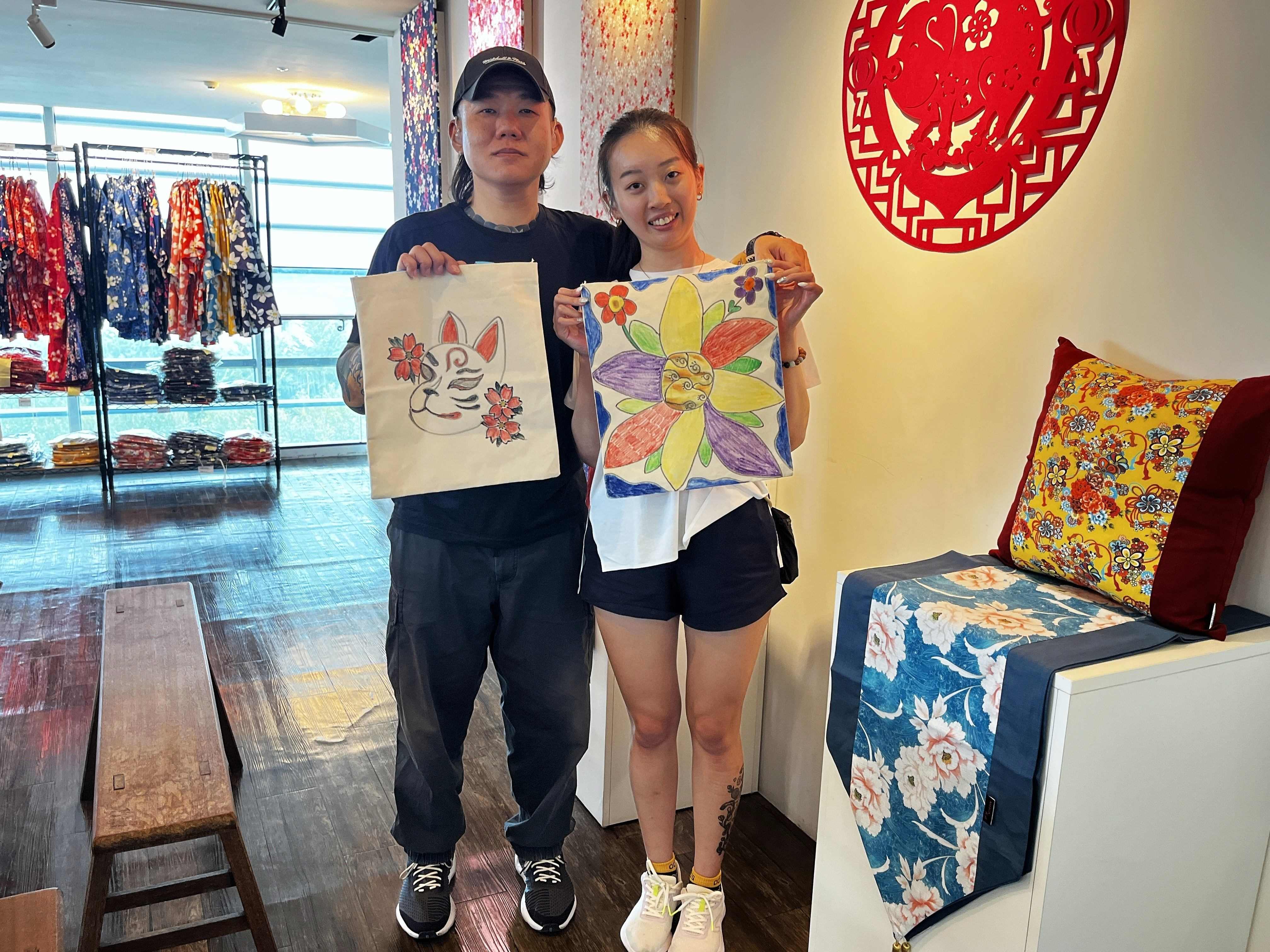聽障情侶吳善暉(左)與吳翊瑄(右)兩人在手譯員的協助下聆聽說明，嘗試彩繪客家花布提袋，留下屬於兩人的旅遊回憶。