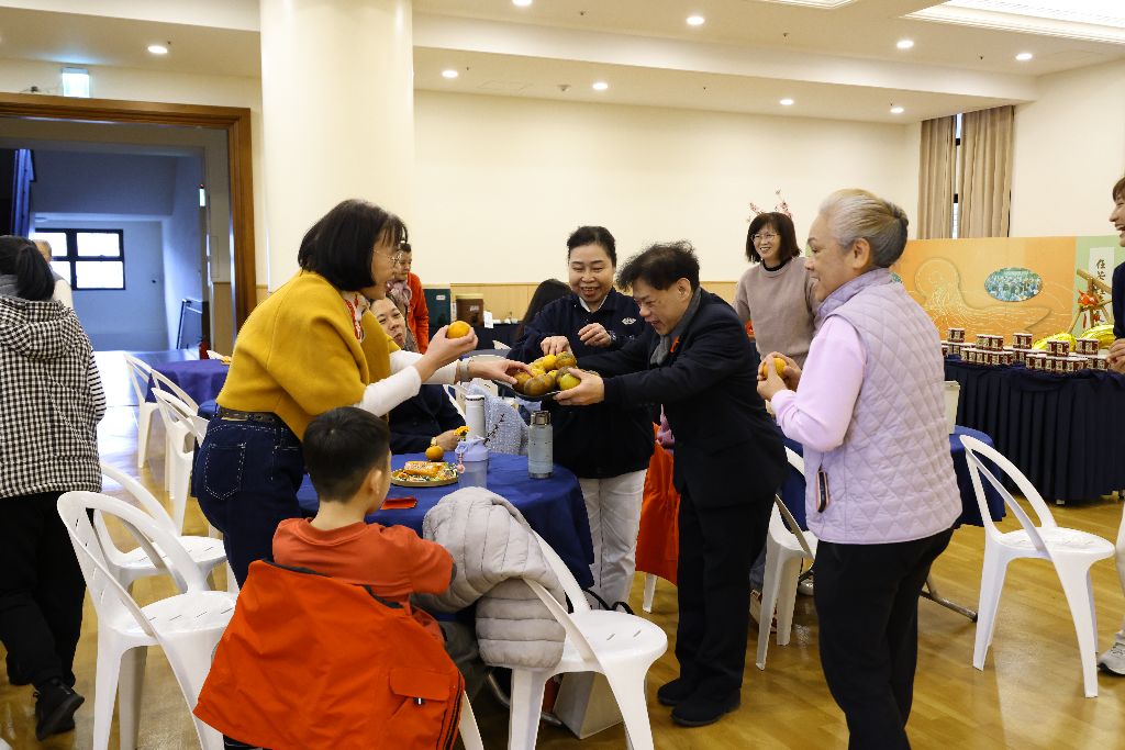 在熱鬧的迎春活動中,志工翁之力(右二)手捧一盤黃澄澄的橘子,象徵「大吉大利」。司儀郭建忠靈機一動,帶動全場稱其為送吉利的「善橘童子」。