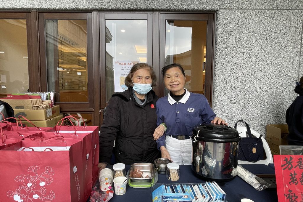 「呷菜熊蓋讚」攤位前熱鬧溫馨。年約八十歲上下的志工林鳳嬌與林謝淑美,每年歲末祝福活動總是義不容辭,熱心推廣花蓮靜思精舍師父手作的淨斯產品,與會眾廣結善緣。