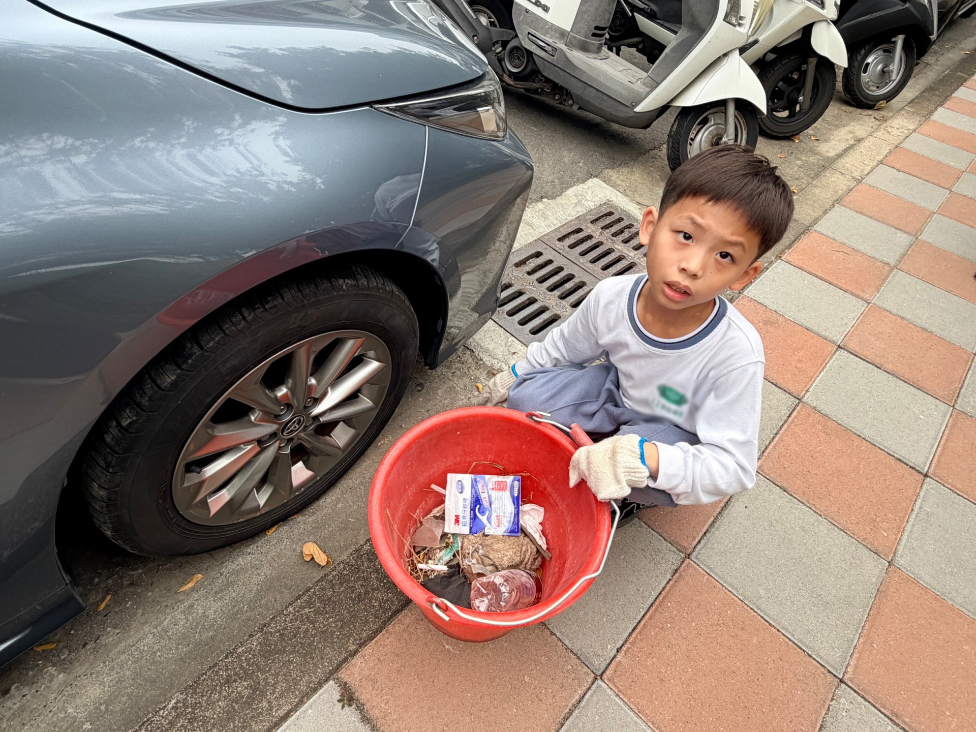孩子專注撿拾汽車底部的菸蒂,細小紙屑也不放過。