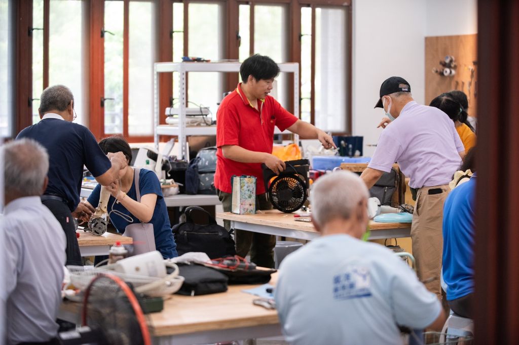 鳳山靜思堂西102生生家電室熱鬧滾滾。桌面上擺放著待修的電風扇、小家電與各式工具設備，志工專注拆解、檢測、清潔與組裝，工具聲與笑聲交織，現場充滿學習與陪伴的溫暖場域。