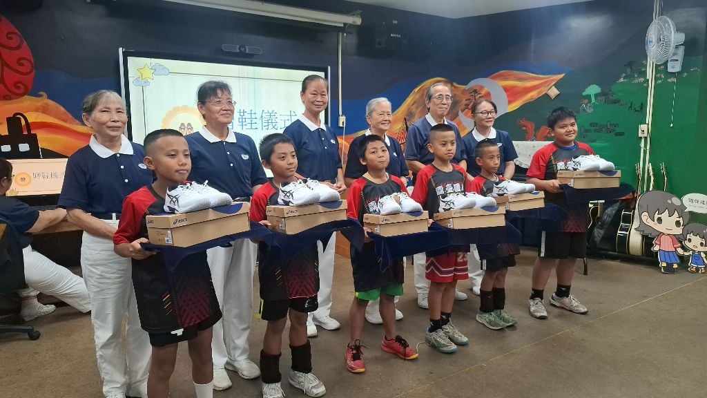 在志工吳雅玲引導下,十二位小朋友分組上台接受球鞋。志工們將鞋子一雙雙放進孩子手中,也將滿滿祝福送進孩子心裡,期待他們穿著新鞋,在球場上勇敢奔跑、奮力拚搏。