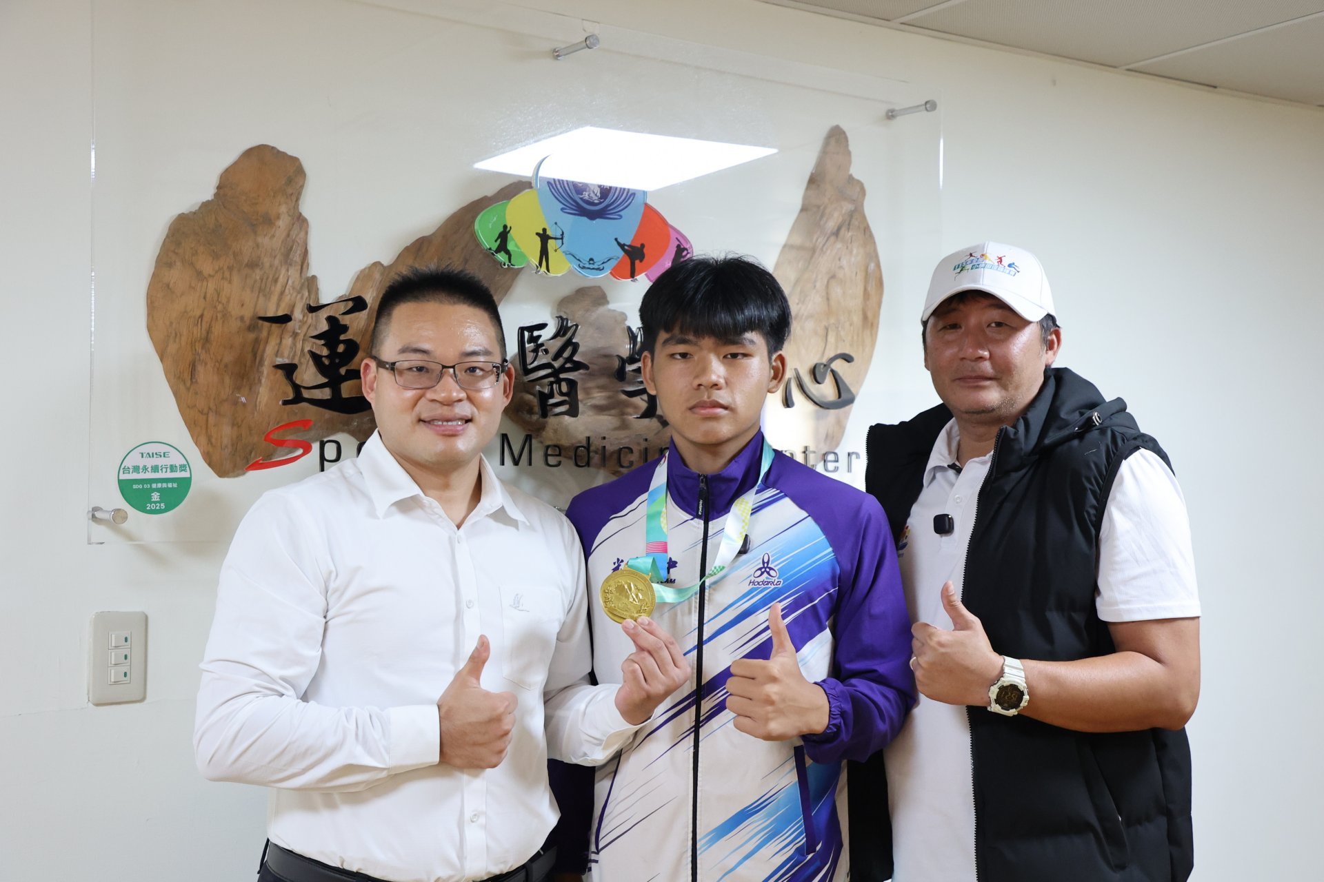 花蓮光復國中標槍選手田佳恩(中)與教練陳緯皓(右),帶著金牌特別回到花蓮慈濟醫院分享榮耀,向一路陪伴他走過傷痛、治療與復健歷程的醫療團隊表達感謝,左為運動醫學中心主任劉冠麟。